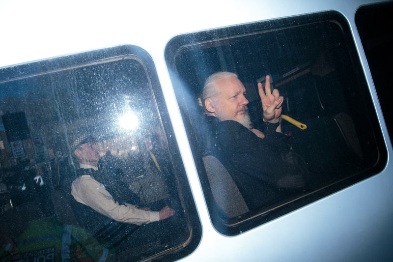 Julian Assange gestures to the media from a police vehicle on his arrival at Westminster Magistrates court on April 11, 2019 in London, England